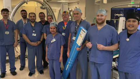 University Hospital Southampton Ten people in surgical scrubs uniform in an operating theatre. One holding a long box which contains the tube used to insert the pacemakers. 