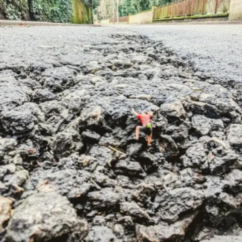 Dave Fargher Miniature mountain climber figures placed inside a pothole, pictured as though they are climbing a mountain