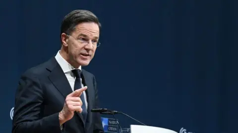 Reuters Mark Rutte, wearing a dark suit and tie and a white shirt, points with his right hand as he delivers a speech at a podium with two microphones , and dark blue background