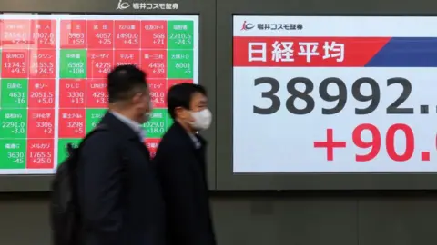 Pedestrians walk past an electronic board displaying the price of the Nikkei stock average outside of a securities firm on 21 January, 2025 in Tokyo.