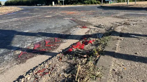 Clare Worden/BBC El ketchup cubre el barro al costado de la carretera y hay marcas de neumáticos en un tramo de la misma.