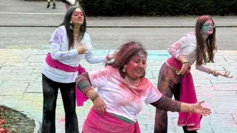 Caroline James Photography Bollywood dance group performing during Holi celebrations. Three women wearing hot pink and white are dancing in Stanley Park with pink powder covering them.