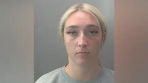 Cambridgeshire Police A custody photo of a blonde woman in a grey T-shirt and fake eyelashes