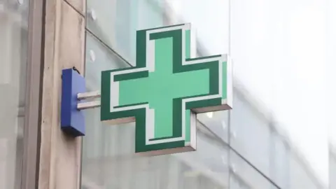 A green cross pharmacy sign attached to a building