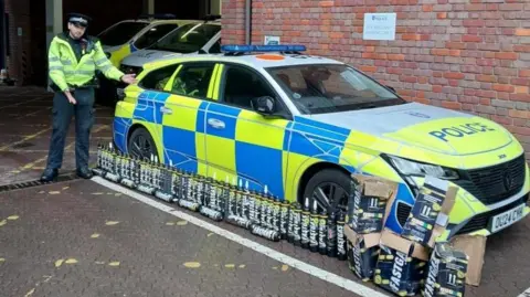 A police officer stood next to a police car with a range of NOS canisters on the ground
