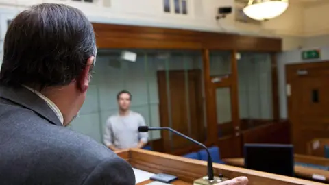 Rear view of male magistrate with dark hair addressing a young man in the dock