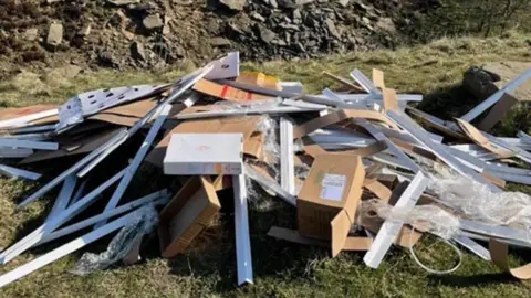 A pile of dumped construction waste - white panels, cardboard boxes and plastic wrap