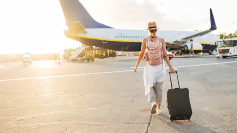 A woman with a suitcase walks towards a passenger aeroplane