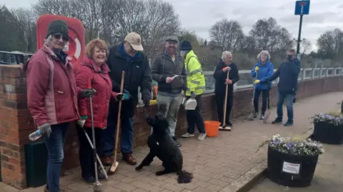 Steve Dunwell A group of people carrying brooms to help clean up the pavements in the community. 