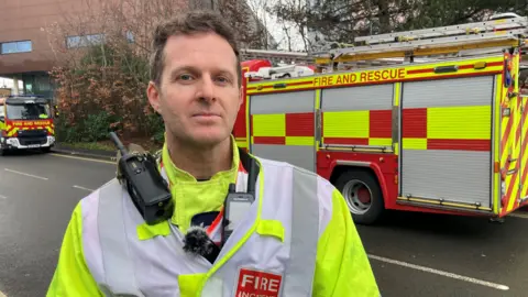 The fire rescue's group manager Larry Mackrell on the street. There are two fire engines behind him.