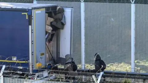 Migrants climbing into the back of a stationary lorry