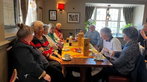 Members sitting on a table with cups of tea and coffee on a table