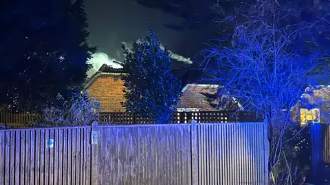 Dan Jessup Smoke seen billowing from the top of the house fire in Frenches Farm Drive, Heathfield. Also visible is a blue silhouette from an emergency service vehicle in attendance.