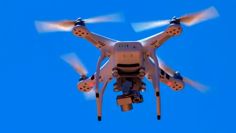 Mark Newman / Getty Images A generic image of a white domestic drone quadcopter in a blue sky. The drone is equipped with a silver camera underneath it