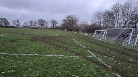 A view across football pitches with muddy tyre tracks visible running in several directions