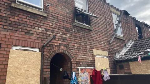 Simon Spark/BBC Shot of the rear of a property with boarded up windows and what appears to be smoke damage on the upper floor. There are clothes hung out on a washing line.