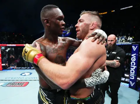 JEFF BOTARI / GETTY IMAGES Dricus Du Plessis dari Afrika Selatan dan Israel Adesanya dari Nigeria berpelukan dan berbicara di atas ring.