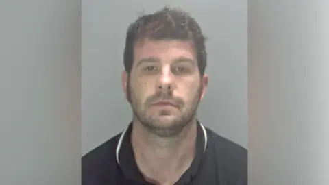 Stuart Worby, pictured in a black or navy-coloured polo shirt, posing for a police custody photo