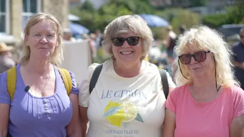 Jamie Niblock/BBC Lynne Sawyer, Debbie Saxby and Carol Alder, who are standing outside Westleton Village Hall. They are all smiling. Lynne is wearing a purple T-shirt, Debbie a white T-shirt and Carol a pink T-shirt.