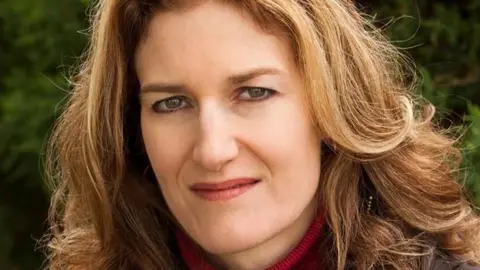 Supplied by PolySeSouvient Heidi Rathjen looks straight ahead at the camera. She is wearing a red turtleneck sweater. 