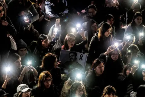  Yuri CORTEZ/AFP A group of young people light cell phones in the darkness of night. One person holds a large black and white picture of the singer Liam Payne