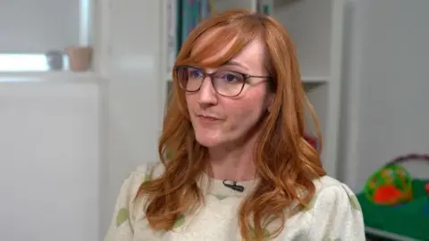 Kris Koth. She has long red hair and has black-framed glasses.