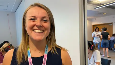 Zac Sherratt/BBC Georgie Cave, associate director of applicant services at Royal Holloway. Georgie has long fair hair and is smiling to camera. Georgie is wearing a black sleeveless top.