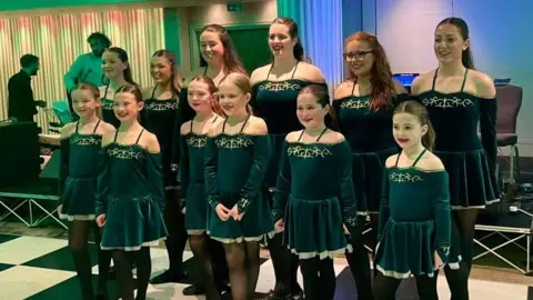 A group of dancers all dressed in dark green clothes.