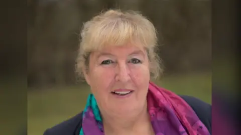Sue Wyeth-Price A headshot of a blonde woman wearing a colourful scarf.