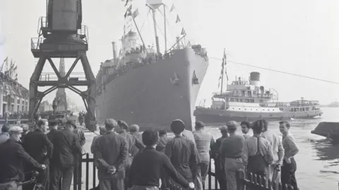 Southampton City Council Archive image of a ship coming into docks in Southampton with dock workers looking on