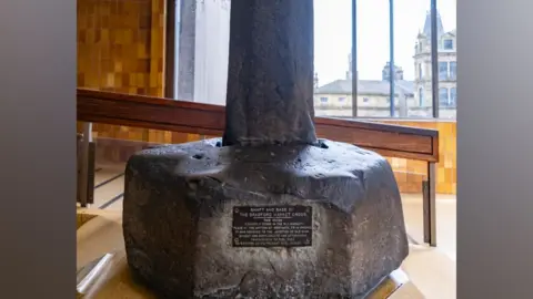 LDRS A large stone base of a cross, displayed on a plinth with a plaque.