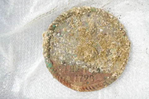 Orkney Museums, Orkney Islands Council A round, metal, rusty object with 1798 enscribed at the bottom.