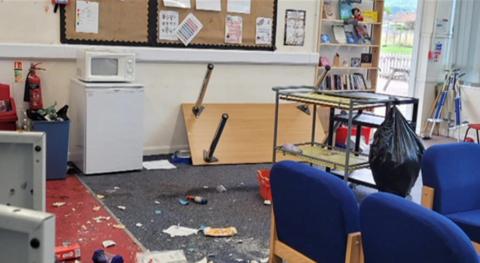 A smashed up classroom, with a table pushed over, stuff all over the floor, looking in a general state
