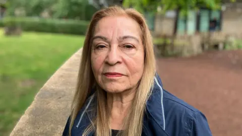 Nahid Ashby looking straight at the camera. She has long straight light brown hair, and is wearing a blue jacket.