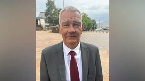 A man in a suit. It is grey and his tie is red. 