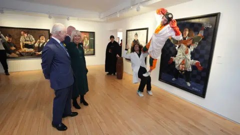 PA Media The King and Queen watch circus performers Mr H and Igor who are depicted in a portrait during a visit to the Sea Holly Gallery in Belfast on the first day of their visit to Northern Ireland.