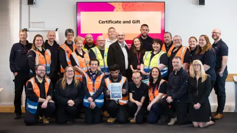 Sam Carpenter A team of twenty five employees are presented with a certificate.