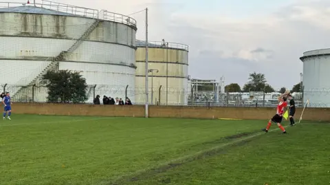 Players on pitch adjacent to petrol depot