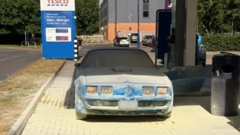 Alan Mutton A fire damaged blue pontiac firebird. It has lost much of its colour and is grey, and covered in the contents of fire extinguishers.