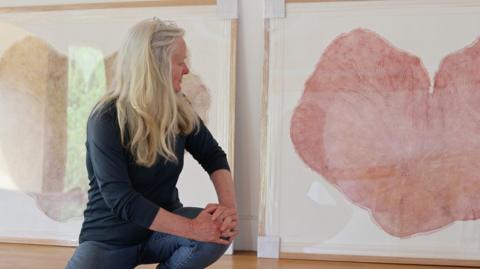 An artist kneeling in front of two large heart shaped images of wood engravings 