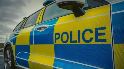 A close up shot of the side of a Northumbria Police car. It is patterned with blue and yellow squares.