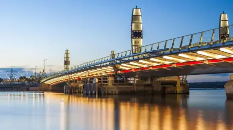 The Twin Sails Bridge at dusk. Lights are reflected in the water.