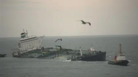 Getty Images The Sea Empress pictured listing to side, with tug boats on either side