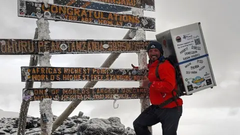 Michael Copeland Michael Copeland carrying a fridge at the summit of Mount Kilimanjaro