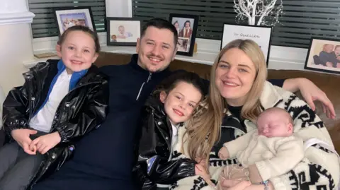 Georgina Gale with her partner Jonny and her three children sitting on a sofa, smiling in the camera 