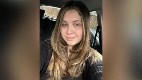 Samantha Field A woman with long brown hair takes a selfie in a car.