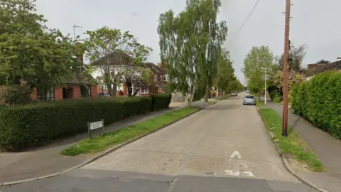 Google Chelmerton Avenue, showing a road, road sign, green verges either side, hedging around front gardens and detached houses 