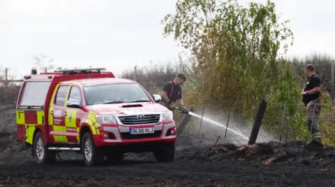PA Firefighters dampen down a field next to burnt out houses