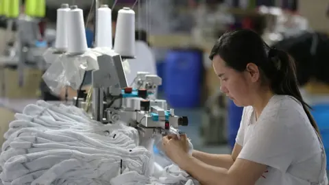 A woman wearing a white T-shirt works in a factory