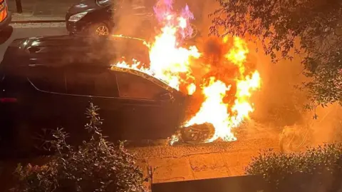A still from a video showing a car on fire. 